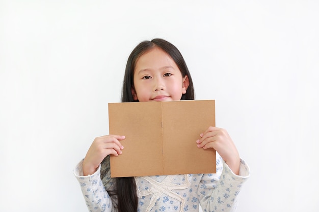 Niña asiática feliz sosteniendo un libro marrón abierto con mirando a la cámara sobre fondo blanco de estudio