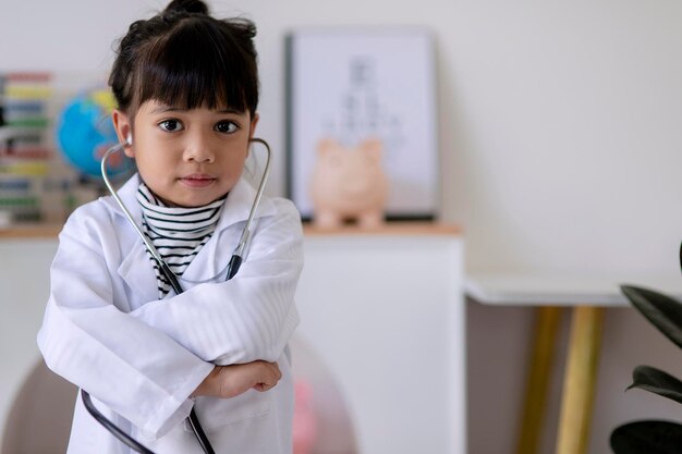 niña asiática con gafas y uniforme médico blanco sostiene un estetoscopio en la mano y quiere realizar un examen juega médico y hospital niño feliz actúa como médico que examina a alguien