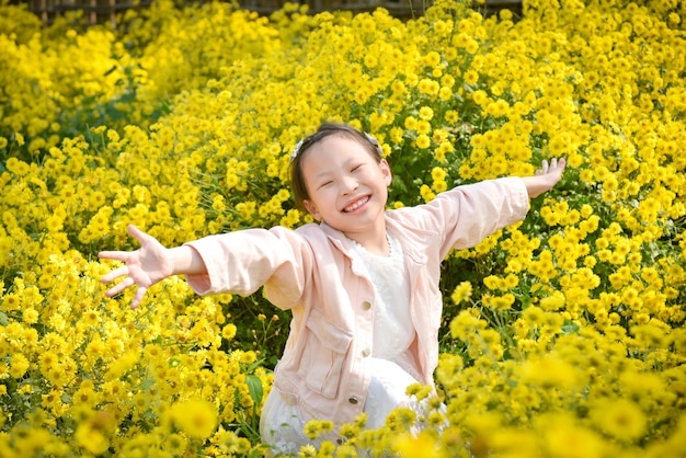 Niña asiática hermosa joven sonriendo y levantando las manos en el campo de crisantemo amarillo.