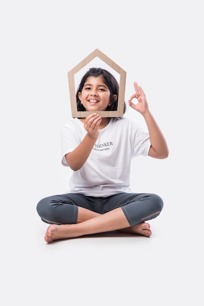 Niña asiática india sosteniendo el modelo de casa de papel contra el fondo blanco - concepto de hogar y familia