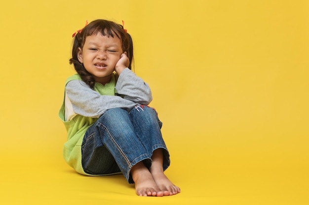 Niña asiática infeliz que sufre de dolor de muelas tocando la mejilla Concepto de cuidado dental