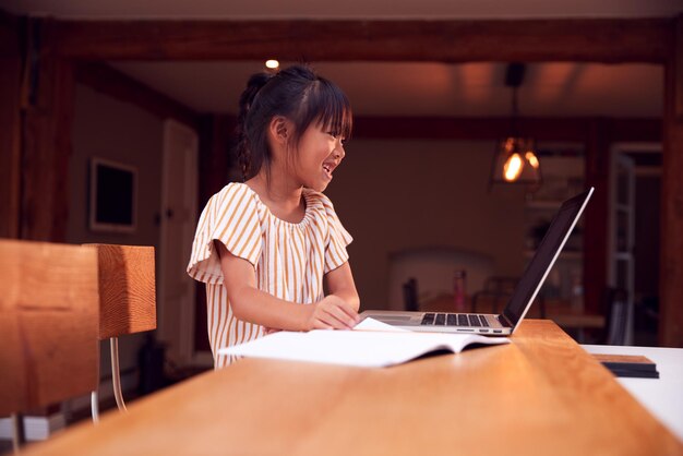 Niña asiática joven escolarización en el hogar trabajando en la mesa usando una computadora portátil