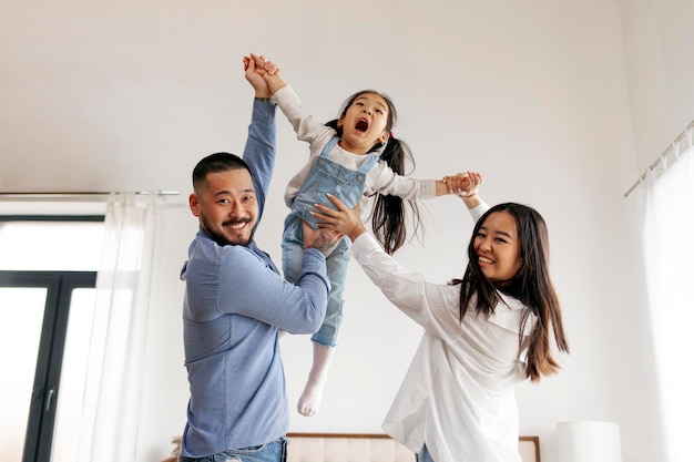 Niña asiática juega con mamá y papá en casa en la habitación padres crían a su hija