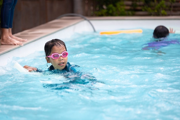 Niña asiática jugando al agua y nadando en la piscina con su amiga con diversión. Actividad de verano y concepto de estilo de vida infantil.