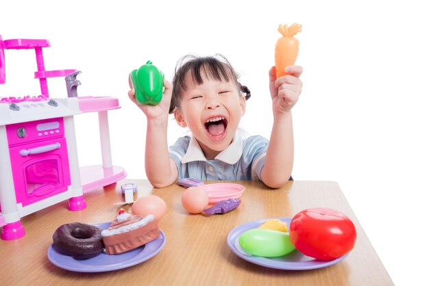 Niña asiática jugando con juguetes de cocina sobre fondo blanco