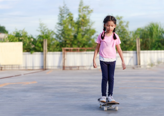 Niña asiática jugando patineta y sonríe con felicidad otra vez cielo azul