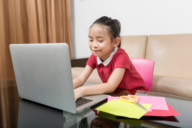 Niña asiática con laptop asistiendo a clases de escuela en línea en casa. Educación en línea durante la cuarentena