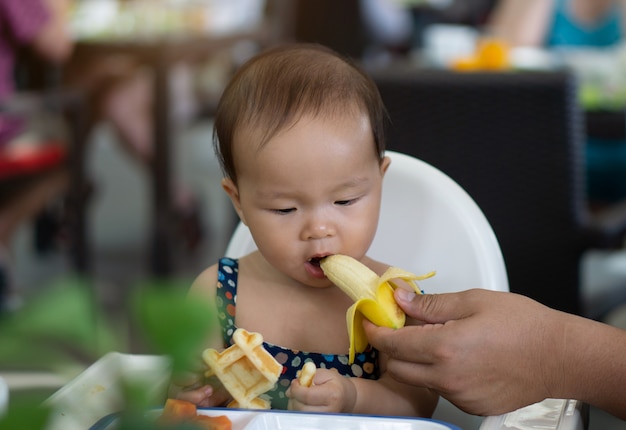 Niña asiática linda del bebé que come el plátano