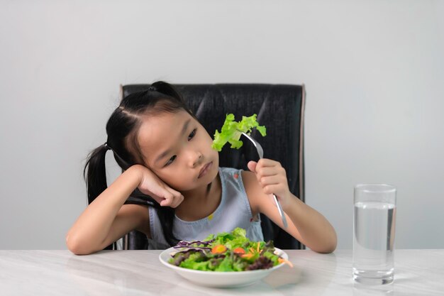 Niña asiática linda se niega a comer verduras saludablesNutrición hábitos alimenticios saludables para niños conceptoA los niños no les gusta comer verduras