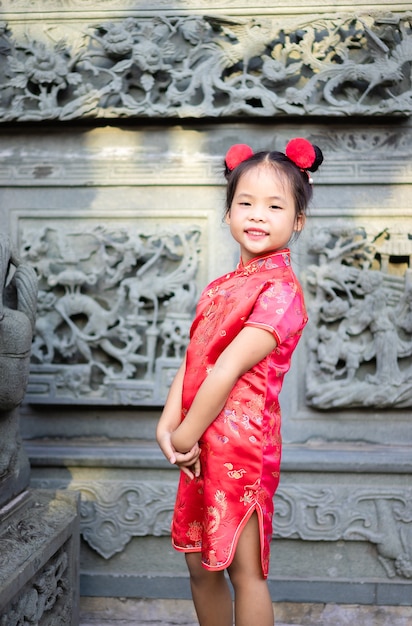 Niña asiática linda en traje tradicional chino sonriendo y de pie en el templo.