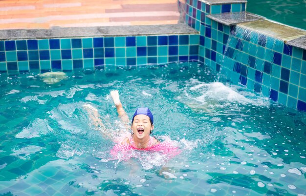 Niña asiática con mangas inflables jugando en la piscina