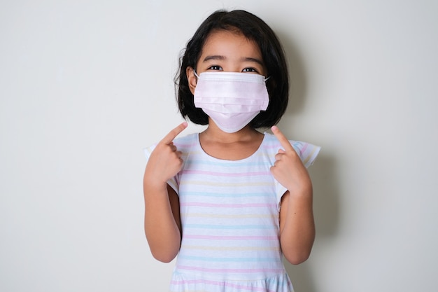 Niña asiática con máscara médica protectora y sus dedos apuntando sobre ella