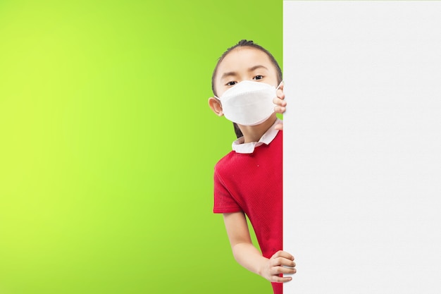 Niña asiática con la máscara de pie junto a la pared con fondo verde