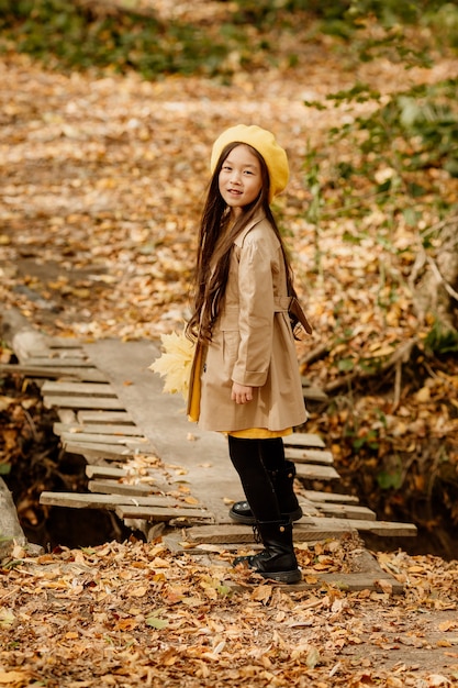 Una niña asiática morena en ropa de otoño camina en el bosque de otoño cerca de un arroyo