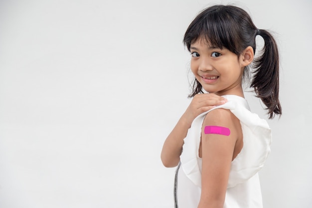 Niña asiática mostrando su brazo después de vacunarse o inocularse, inmunización infantil, concepto de vacuna covid delta