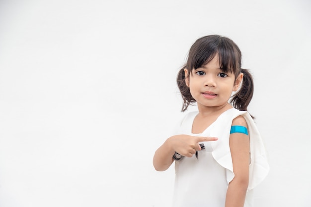 Niña asiática mostrando su brazo después de vacunarse o vacunarse la inmunización infantil