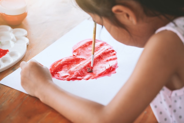 Niña asiática niño dibujo y pintó un corazón para la tarjeta de San Valentín con diversión y felicidad