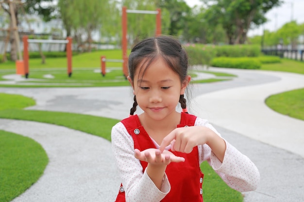 Niña asiática niño gesto dedo tocar algo y mirando sin tema en las manos mientras está en el jardín