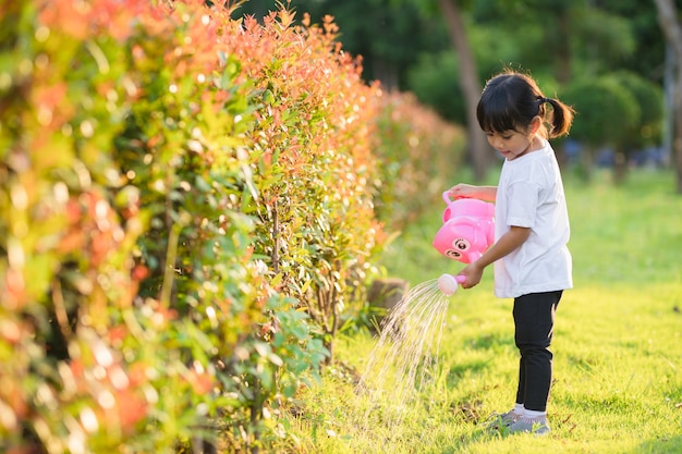 Niña asiática niño vertiendo agua sobre los árboles. El niño ayuda a cuidar las plantas con una regadera en el jardín.