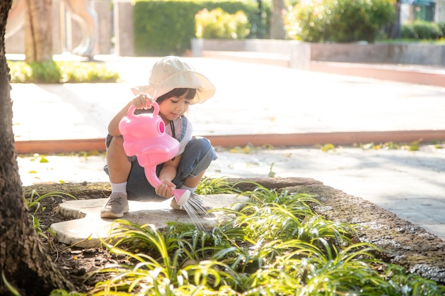 Niña asiática niño vertiendo agua sobre los árboles. El niño ayuda a cuidar las plantas con una regadera en el jardín.