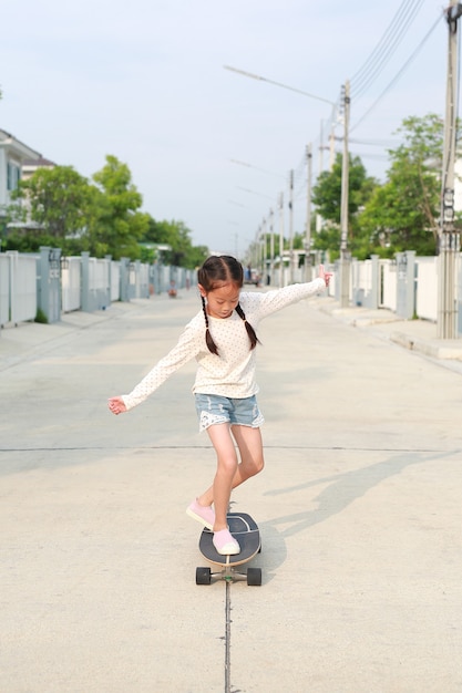 Niña asiática patinando en patineta en la calle