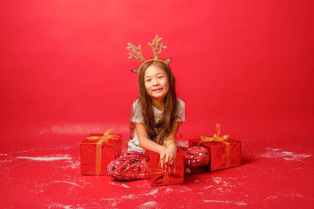 Niña asiática en pijama sobre un fondo rojo con regalos