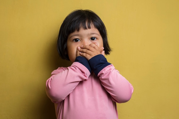 Niña asiática puso su mano cerca (cubriendo) su boca