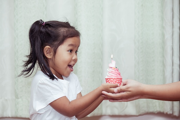 niña asiática que se divierte a soplar cupcake de cumpleaños en tono de color vintage