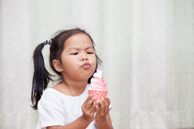 niña asiática que se divierte a soplar cupcake de cumpleaños en tono de color vintage