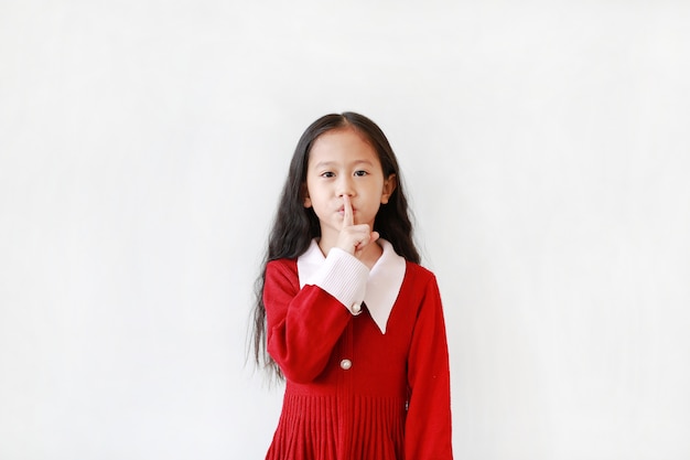 Niña asiática que guarda silencio sobre el fondo blanco