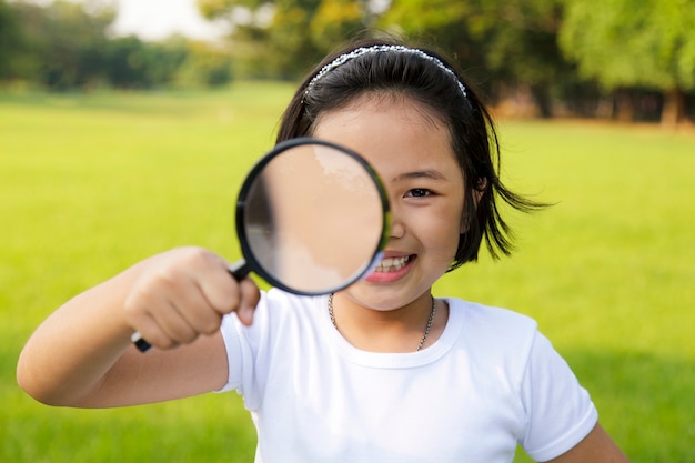 Niña asiática que sostiene una lupa en al aire libre