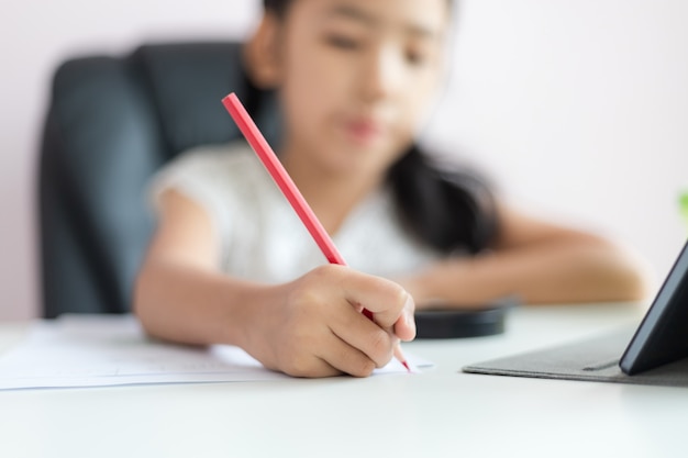 Niña asiática que usa el lápiz para escribir en el papel haciendo la tarea para el concepto de educación