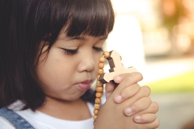 Niña asiática rezando sosteniendo la cruz, concepto cristiano.