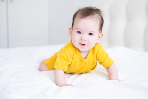 Una niña asiática saludable de 5 meses con traje amarillo en la cama con ropa de cama blanca