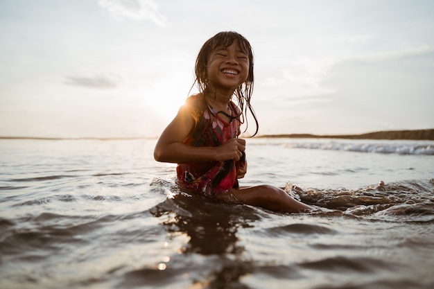 Niña asiática sentada en la arena en la playa mientras juega con agua