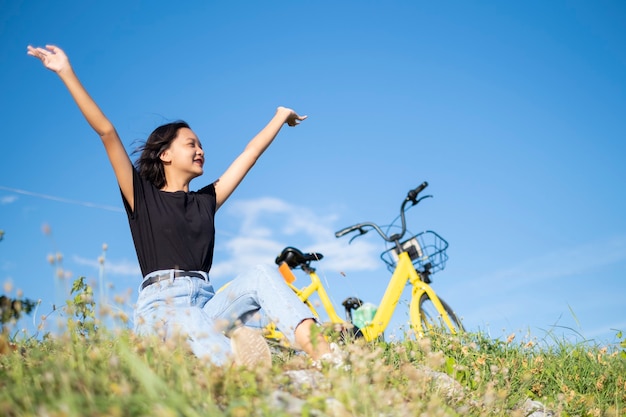 Niña asiática sentada con bicicleta yallow en el parque con cielo azul