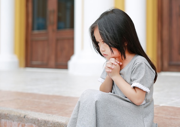 Niña asiática sentada y rezando en la iglesia