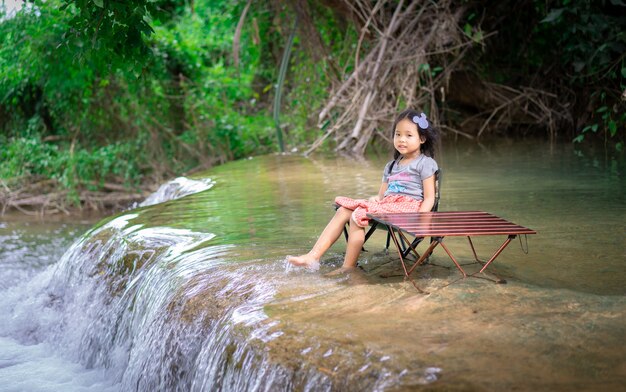 Niña asiática sentada en una silla en la cascada entre acampar