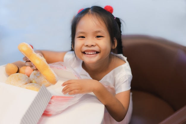 Niña asiática sentada en la silla con tenencia y comer donas