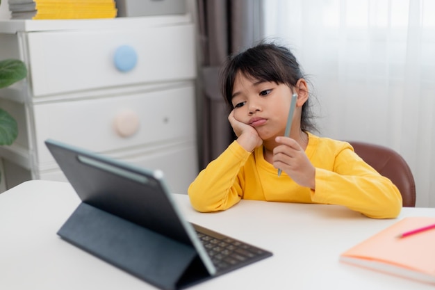 Niña asiática sentada sola y mirando hacia afuera con una cara aburrida Niño preescolar acostado cabeza abajo en la mesa con triste aburrido con la tarea niño malcriado