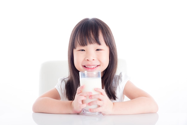 Niña asiática sentado y sosteniendo un vaso de leche sobre fondo blanco