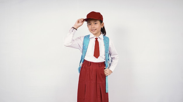 Niña asiática con sombrero y mochila escolar sonriendo felizmente sobre fondo blanco aislado