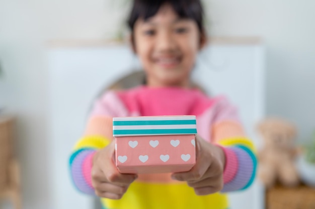 Niña asiática sonríe y emocionada y sosteniendo una caja de regalo roja en el fondo de la sala de estar. niño con caja de regalo en Navidad y año nuevo. Sonrisa y sorpresa de niña asiática.