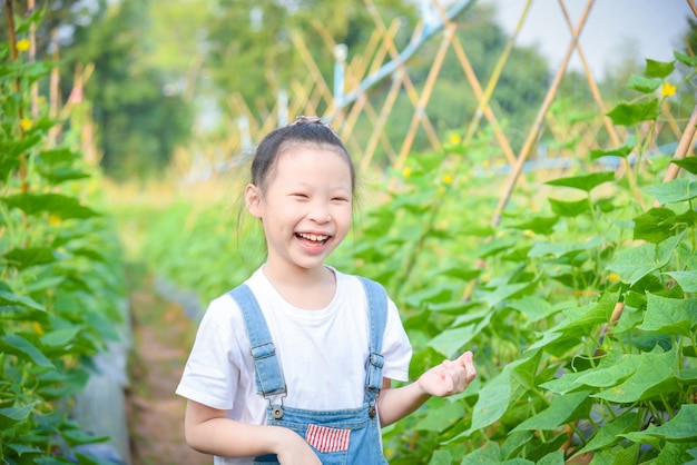 Niña asiática sonriendo en el jardín de pepinos.