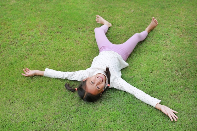 Niña asiática sonriente tumbada en el césped verde en el jardín