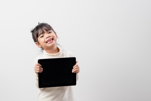 Niña asiática sosteniendo y usando la tableta digital en el espacio de copia libre de fondo de estudio blanco