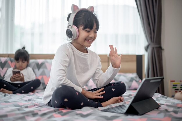 Niña asiática tomando clases en línea y feliz por el concepto de pandemia de coranavirus en cuarentena de Homeschool