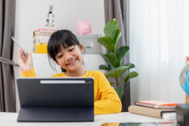 Niña asiática tomando clases en línea y feliz por el concepto de pandemia de coranavirus en cuarentena de Homeschool