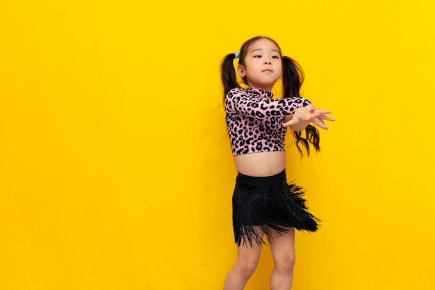 Niña asiática en traje de baile baila chachacha sobre fondo amarillo aislado bailarina coreana infantil