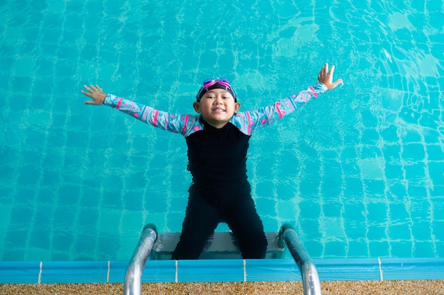 Niña asiática con traje de baño y gorra con gafas en el borde de la piscina Aprende a nadar el concepto de idea